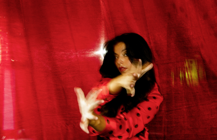 Mujer morena vestida de rojo con lunares, bailando sobre fondo rojo