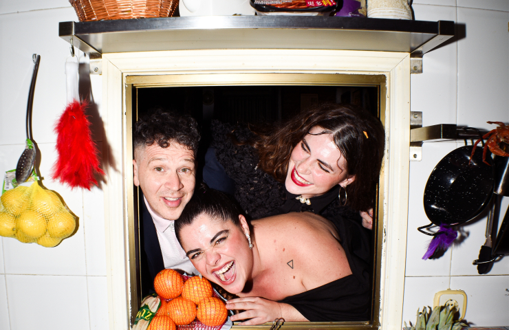 Tres personas riéndose asomadas a una ventana en una cocina