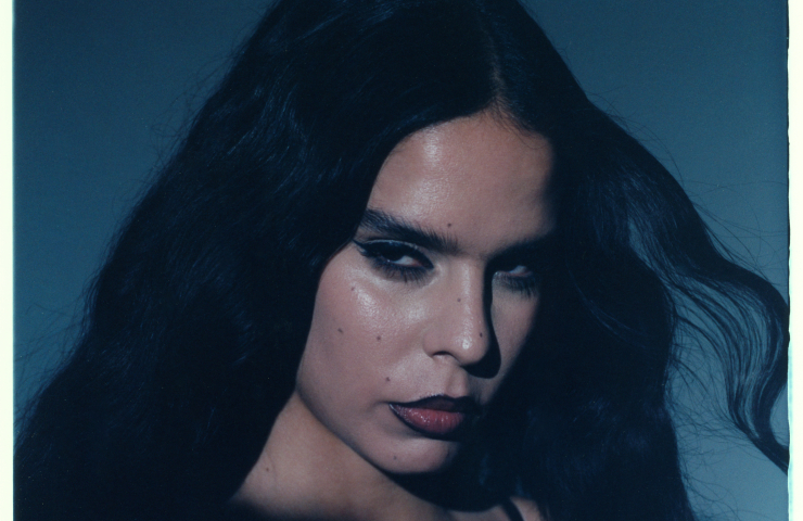 Primer plano de mujer morena, mirando de lado, sobre fondo azul oscuro