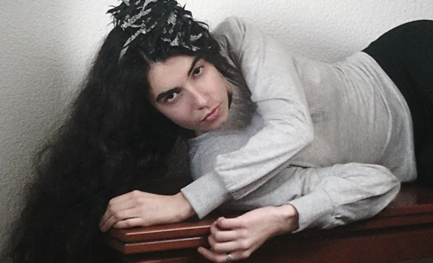 chica con pelo largo moreno, lazo en la cabeza tumbada de manera lateral sobre un mueble de madera