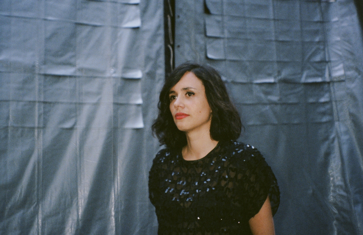 Mujer de medio lado vestida de negro sobre fondo de tela gris