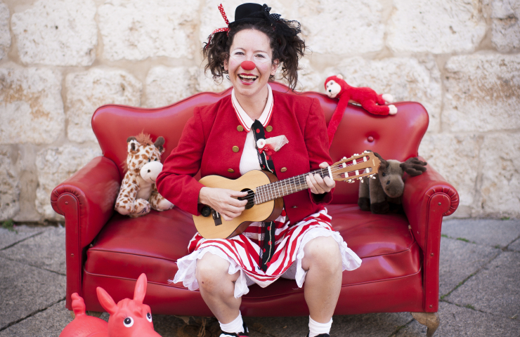 payasa sentada en su sofá rojo en la calle con un ukelele entre las manos