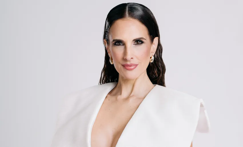 mujer de frente, pelo largo peinado hacía atrás, blusa blanca con gran escote, maquillada, pendiente dorados
