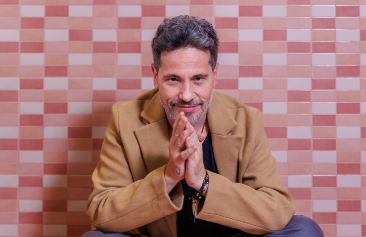 Hombre con cazadora de ante sentado frente a pared de ladrillos rojos