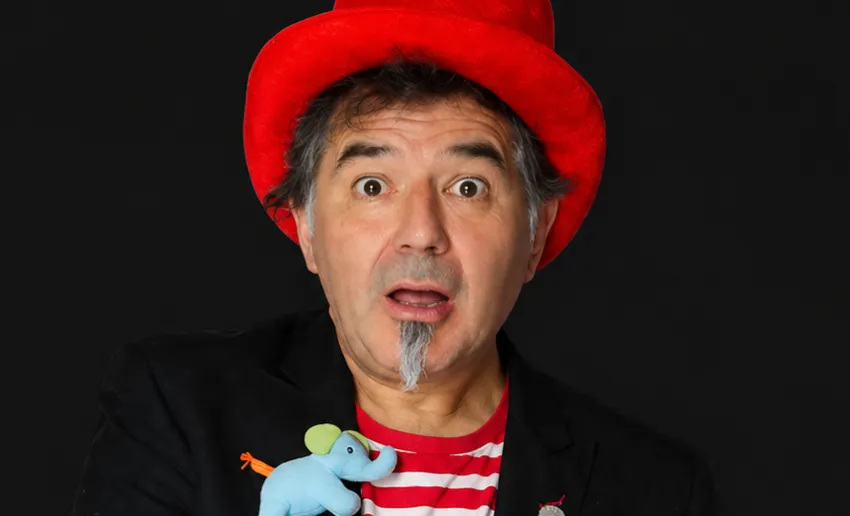 hombre con pequeña perilla y cara de sorpresa, sombrero rojo, camiseta de rayas blanca y roja, chaqueta negra, y broche